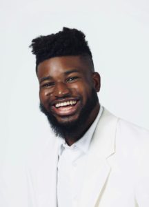 It is a headshot of Fikayo Aderoju smiling wearning an all white outfit in front of a white background