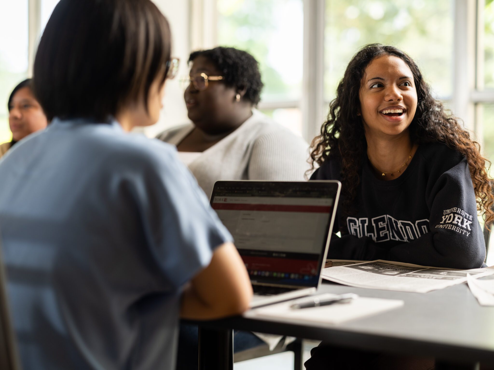 Students sitting at a table with a laptop and smiling