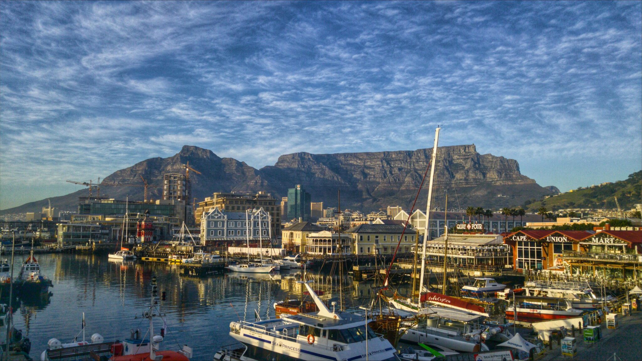 V&A Waterfront, Cape Town: Harbor scene at Cape Town’s V&A Waterfront with boats, shops, and Table Mountain in the background.